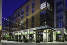 An image of a multifamily building with commercial spaces on the ground floor. The image is taken at night. The brown building has Nichiha VintageWood and is seen from street level.